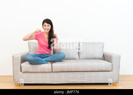 lächelnde Schönheit Dame mit Zahnbürste ihre Zähne zu reinigen, nachdem sie essen Donut auf Sofa sitzen und Blick in die Kamera mit weißem Hintergrund. Stockfoto