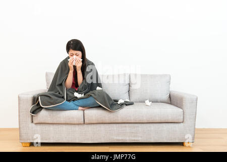 junge Schönheit Frau sitzend auf Sofacouch im Holzboden und mit Seidenpapier weht Nase schniefen wenn sie eine Erkältung mit weißem Hintergrund. Stockfoto