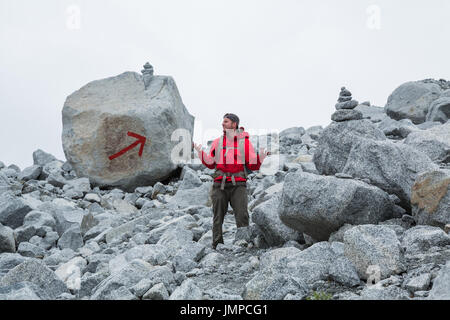 Der Weg ist markiert mit zwei großen Cairns und ein riesiger roter Pfeil auf einen Felsen gemalt, aber dieser Mann scheint verloren zu sein. Grauen, bewölkten Himmel Stockfoto