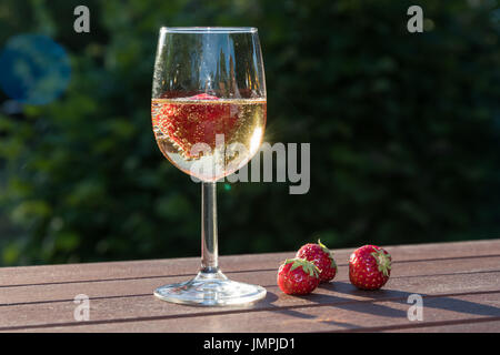 Erdbeeren und ein Glas Sekt auf einem Holztisch im Garten Stockfoto