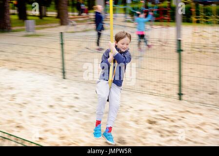 Der junge ist auf dem Spielplatz rutschen ein Seil Stockfoto