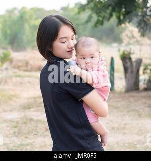 Porträt der jungen Mutter hält ihr kleines Baby Blick in die Kamera und zeigt den Mittelfinger Stockfoto