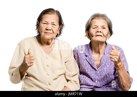 Porträt von zwei senior asiatischen Frauen sitzen auf der Couch und Daumen auftauchen. Isoliert auf weißem Hintergrund mit Beschneidungspfad Stockfoto