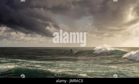 Ein Mann paddle-boarding Surfen eine Welle in Sydneys Nordstrände in den frühen Morgenstunden an einem stürmischen Tag Stockfoto