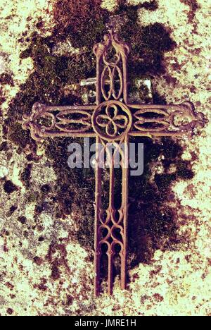 Gebrochene Eisen rustikal Kruzifix auf alten bemoosten Grabstein. Verlassene Symbol der Religion. Stockfoto