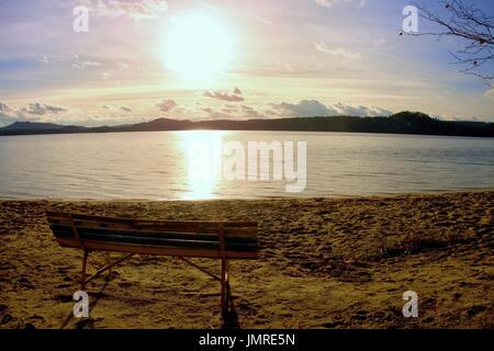 Leere Außenbank auf Herbst Strandbad. Die Küste mit strahlende Sonne auf einem Hintergrund. Vintage getönten Foto mit Lens-Flare-Effekt Stockfoto