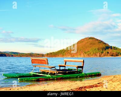 Verlorene alte Tretboot verfing sich auf sandigen Strand bei Sonnenuntergang. Insel mit Waldhügel am Horizont. Stockfoto