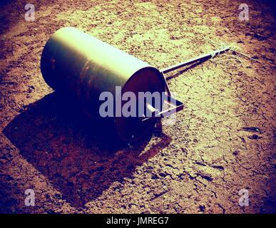 Alten rostigen Eisen Barrel für Wartung Vernachlässigung Tennisplatz. Alten trockenen roten zerkleinerten Ziegelsteinen Oberfläche auf Tennis im freien Boden. Stockfoto