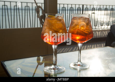 Kellner vorbereitet Aperol Sprits Sommer cocktail mit Aperol, prosecco, Eis-Würfel und Orange im Weinglas, bereit, auf der sonnigen Terrasse mit Meer zu trinken Stockfoto