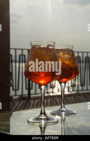 Kellner vorbereitet Aperol Sprits Sommer cocktail mit Aperol, prosecco, Eis-Würfel und Orange im Weinglas, bereit, auf der sonnigen Terrasse mit Meer zu trinken Stockfoto