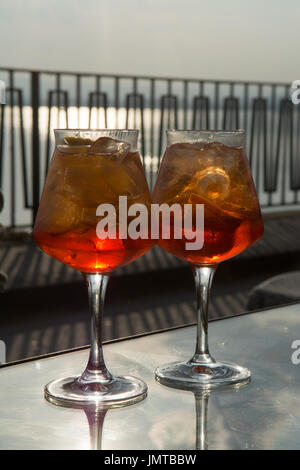 Kellner vorbereitet Aperol Sprits Sommer cocktail mit Aperol, prosecco, Eis-Würfel und Orange im Weinglas, bereit, auf der sonnigen Terrasse mit Meer zu trinken Stockfoto