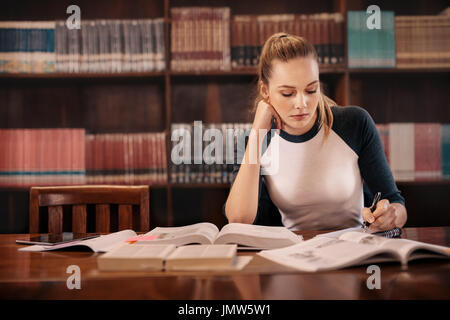 Student, der sich auf die Prüfung in der Bibliothek vorbereitet. universitätsstudent macht Notizen aus dem Buch, während er in der Bibliothek sitzt. Stockfoto