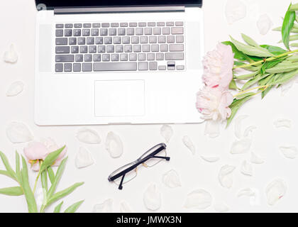 Arbeitsplatz mit Laptop, Gläser und Pfingstrose Blumen auf dem weißen Tisch-Hintergrund. Flach legen, Top Aussicht Stockfoto