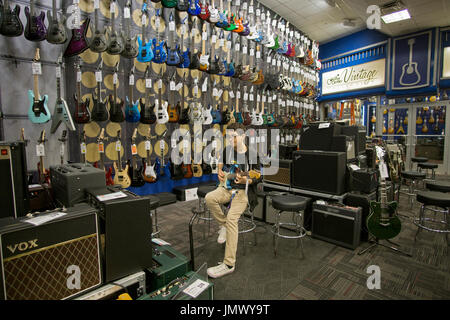 Ein junger Mann Einkaufen für eine Gitarre probiert eine Fender Guitar Center Showroom auf der West 14th Street in Manhattan, New York City. Stockfoto