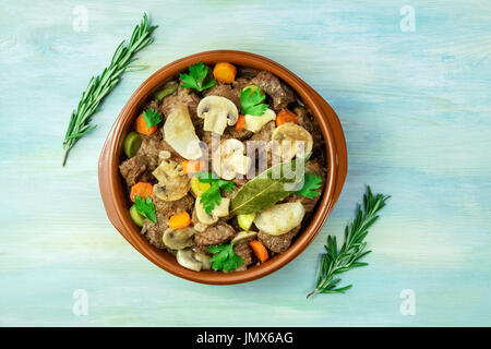 Ein Foto von einem Fleisch-Ragout in einer irdenen Schüssel mit Zweige frischer Rosmarin, geschossen von oben auf eine Hintergrundtextur blaugrün, mit einem Platz für text Stockfoto