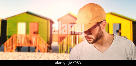 Modell mit Kappe und Sonnenbrille gegen Multi farbige Hütten auf Sand gegen klaren Himmel Stockfoto