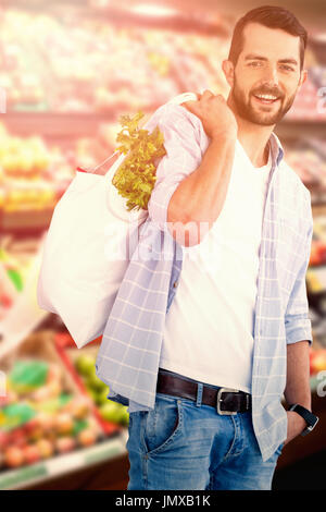 Porträt des jungen Mannes mit Gemüse im Warenkorb gegen Obst im Supermarkt angeordnet Stockfoto