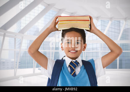 Lächelnd Schüler tragen Bücher über Kopf auf weißem Hintergrund gegen moderne Zimmer mit Blick auf Stadt Stockfoto