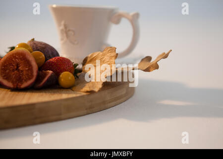 Herbstlaub, verschiedene Früchte und Tee auf Schneidebrett vor weißem Hintergrund Stockfoto