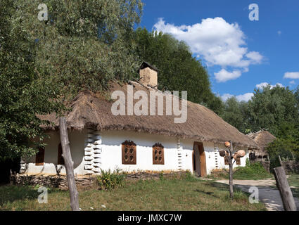 Alte traditionelle ukrainische Landhaus mit strohgedeckten Dach und geflochtenen Zaun im Garten vor einem blauen Himmel mit einer weißen Wolke Stockfoto