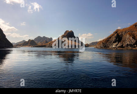 Küste von Bergen mit grüner Vegetation spiegelt sich im blauen Ozeanwasser in Labuan Bajo auf Flores, Indonesien. Stockfoto