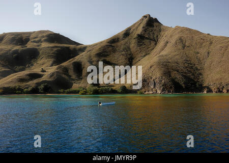 Kleines Boot vor der Küste von Bergen mit grüner Vegetation spiegelt sich im blauen Ozeanwasser in Labuan Bajo auf Flores, Indonesien. Stockfoto