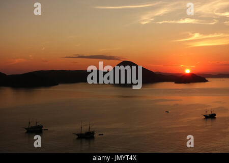 Orange Sunrise Blick von Padar Inselbereich des Komodo National Park mit drei kleinen Silhouette-Boote in den Ozean, Flores Indonesien. Stockfoto