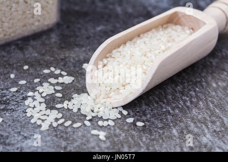 Hölzerne Schaufel mit Pudding Reis und Reis auf eine graue Fläche mit großen Behälter mit Reis im Hintergrund Stockfoto