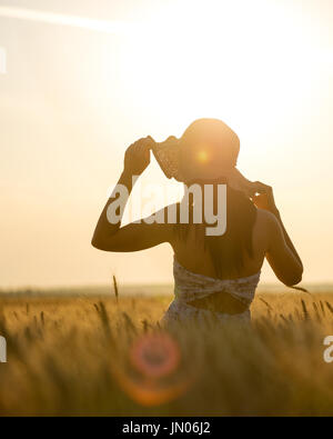 schöne Frau mit Sommerhut in Weizenfeld bei Sonnenuntergang Stockfoto