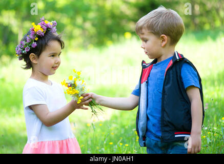 kleiner Junge mit Blumen für ein kleines Mädchen Stockfoto