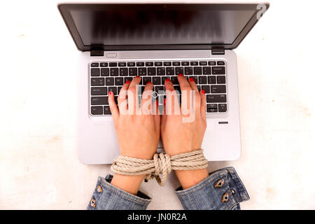 Moderne Sklaverei Konzept. Zarte Frauenhand gebunden arbeiten auf einem Computer am Arbeitsplatz Stockfoto