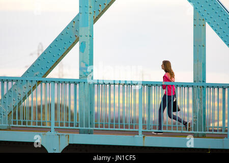 Eine Frau zu Fuß am frühen Morgen über die blauen Jubiläums-Brücke bei Queensferrry, die überquert den Fluss Dee und Mündung in Flinthsire, Wales, UK Stockfoto