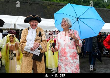 Milton Abbas, Dorset, UK.  29. Juli 2017.  Starkregen nicht Besucher abschrecken, da sie in die Milton Abbas aus dem 18. Jahrhundert Street Fair in Dorset strömen.  Ehemalige BBC-News-Reporter Kate Adie zusammen mit Michael McAvoy trägt historischen Kostümen, mit ihrem Umrella oben vor der Eröffnung der Messeauftritts.  Bildnachweis: Graham Hunt/Alamy Live-Nachrichten Stockfoto