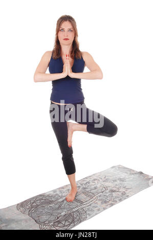 Eine schlanke junge Frau in einem Ausübung Outfit steht auf einem grauen Tuch auf einem Bein mit den Händen gefaltet, für weißen Hintergrund isoliert Stockfoto