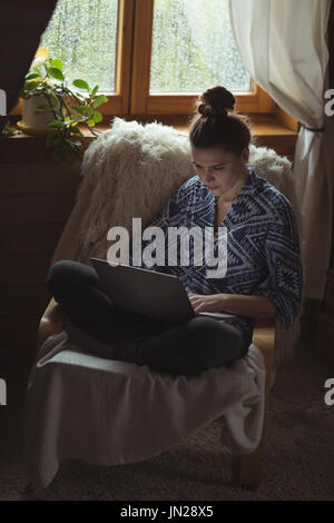 Frau mit Laptop auf Stuhl im Wohnzimmer zu Hause Stockfoto