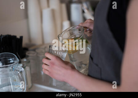 Mittleren Bereich der Frau gießt Wasser in Trinkglas stehend in Küche Stockfoto