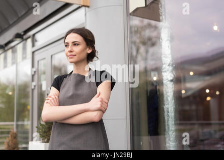 Weibliche Besitzer mit Arme gekreuzt wegsehen stehend im Coffee shop Stockfoto