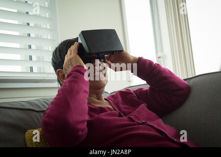 Ältere Frau mit virtual-Reality-Simulator beim Sitzen auf dem Sofa zu Hause Stockfoto
