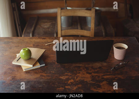 Laptop mit Apfel, Bücher, Brille und Kaffeetasse zu Hause auf Tisch Stockfoto