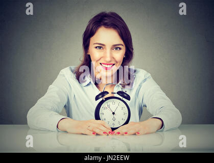 Lächelnde Geschäftsfrau mit Wecker am Tisch in ihrem Büro sitzen. Stockfoto