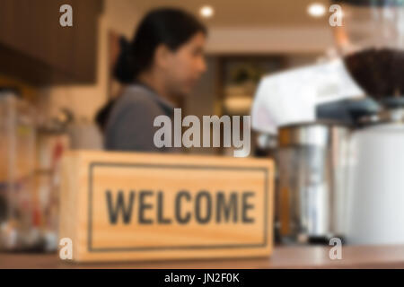Unscharfen Hintergrund der weiblichen Barista bereiten Kaffee trinken hinter hölzernen Willkommensschild im Café oder Coffee-Shop. Stockfoto