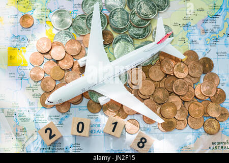 Flugzeug-Figur auf einer Weltkarte und ein Haufen von Münzen und Holz Zahlen 2018 als Reisen, Reise, Reisen nach Reiseziel Hintergrund Konzept. Stockfoto