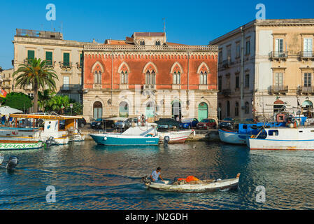 Sizilienstadt, Blick auf einen Fischer, der sein Boot im malerischen Darsena Channel zwischen dem Hafen von Syrakus und der historischen Insel Ortigia, Sizilien, steuert Stockfoto