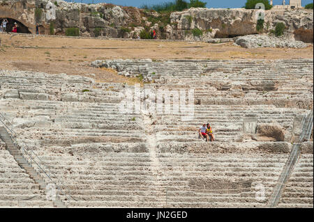 Griechisches Theater in Sizilien, Ansicht eines Paares, das in den Ruinen des Auditoriums eines antiken griechischen Theaters sitzt, Archäologischer Park von Syrakus, Sizilien. Stockfoto