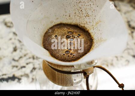 Frisch gebraut schwarzen Kaffee sprudeln in eine weiße Tasse auf einem rustikalen Holztisch, eine Ansicht von oben entnommen. Stockfoto