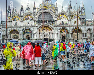 St. Markus Kathedrale Basilika in Venedig Italien an einem regnerischen Tag überfüllt mit Touristen in bunte Regenjacken und Schirme wie Tauben herumlaufen Stockfoto