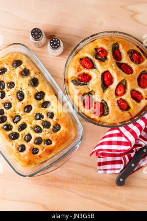 Zwei hausgemachte italienische Focaccia mit Oliven und Kirschtomaten auf einem Holztisch Stockfoto