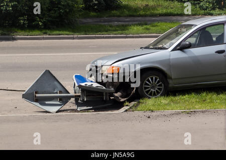 Kaputtes abgestürztes Auto auf der Straße. Geneigten Schild auf einem Fußgängerüberweg Stockfoto