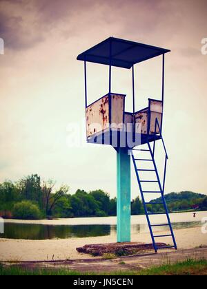 Ein Alter weiß und rostigen Metall Rettungsschwimmer-Turm mit Stuhl an einem Teich-Strand. Stockfoto