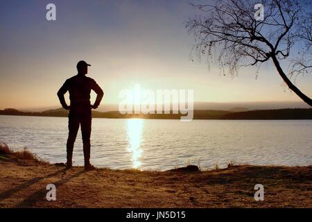 Einsame Sportler farbenprächtigen Sonnenuntergang am Ufer des herbstlichen See betrachten. Mann Stand unten Birke. Stockfoto